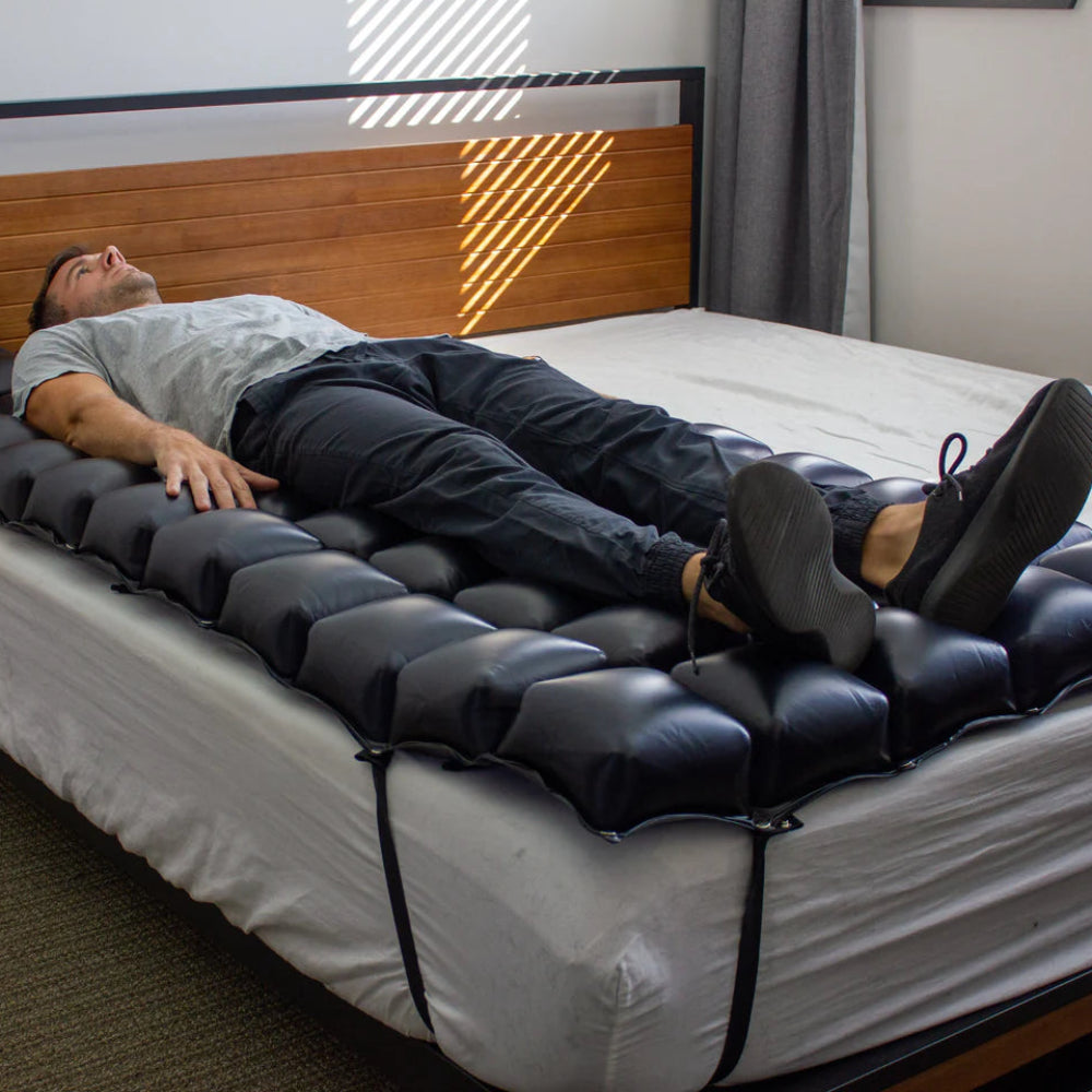 A person lying on the mattress overlay, demonstrating the effective immersion and support provided to the torso and hips to prevent tissue breakdown.