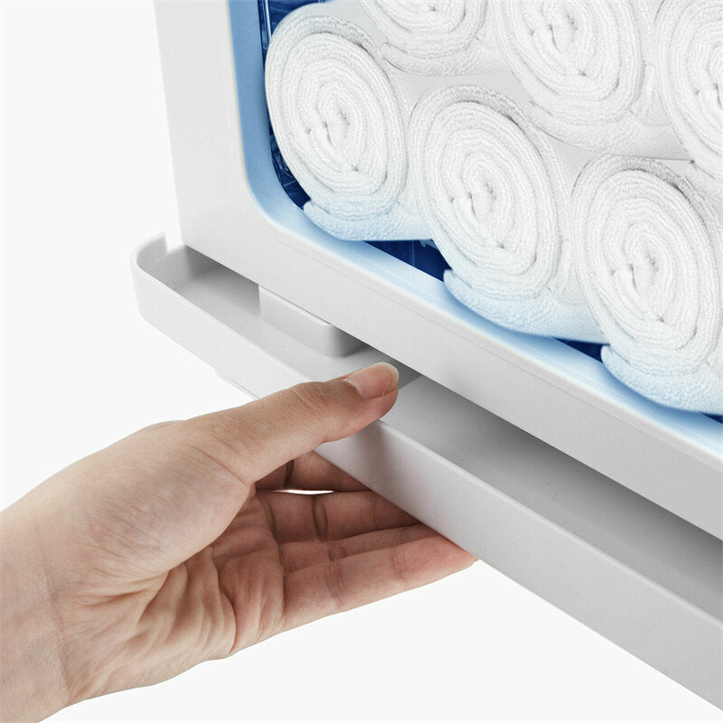 Hand pulling out the removable water drip tray at the bottom of a white hot towel warmer cabinet filled with rolled white towels.