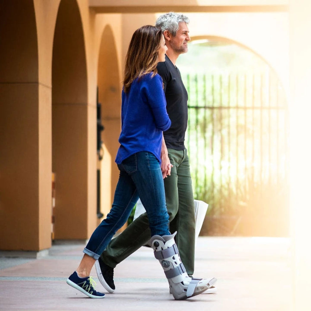 A person using the AirSelect Elite walking boot while walking outdoors, demonstrating the rocker sole's ability to maintain a natural gait.