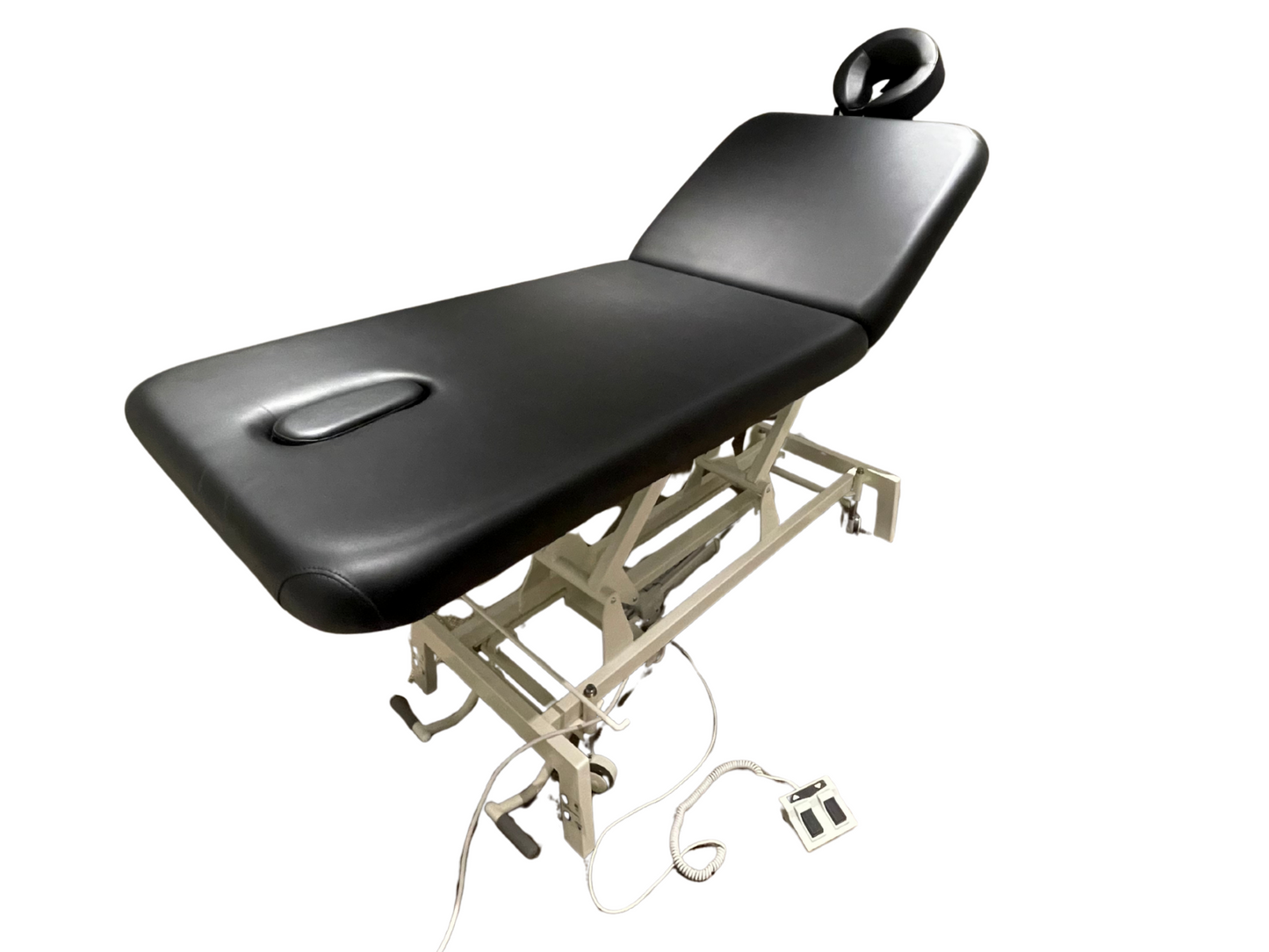 Angled view of the black 2-section electric height control facial massage treatment table in a fully flat position, highlighting its sturdy white scissor-lift base and foot pedal.