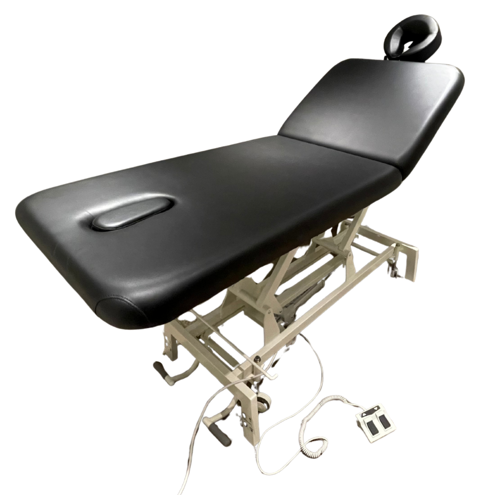 Black 2-section electric facial massage treatment table with adjustable headrest, built-in face hole, and foot pedal control on a white background.