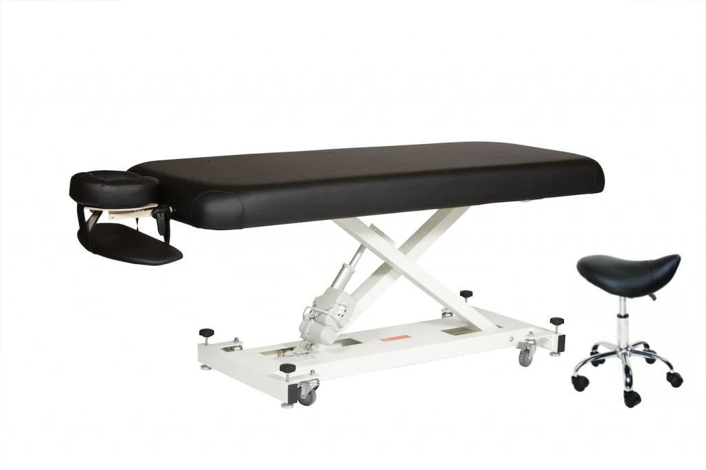 Black padded massage table on a white scissor lift base with castors, shown with a black saddle stool.