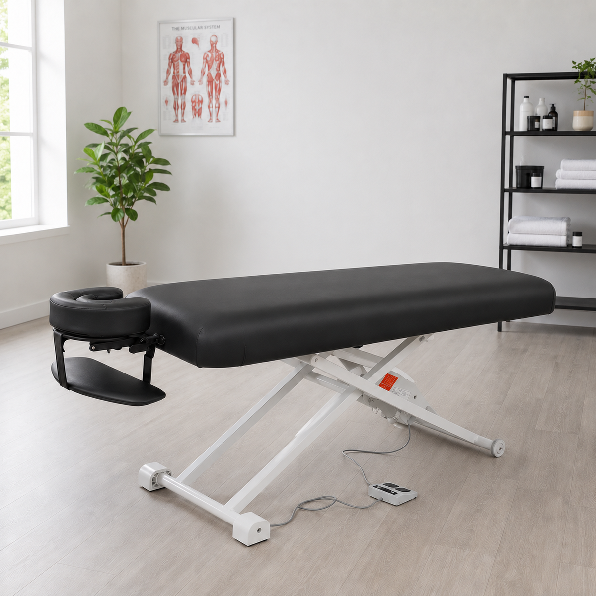 Black electric lift massage table with white steel frame and foot pedal in a bright treatment room with plant and shelving