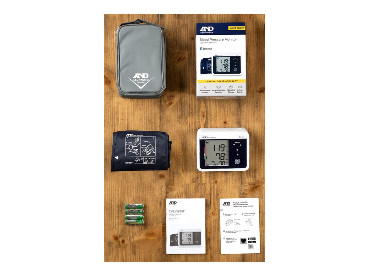 A&D Medical Bluetooth voice-guided blood pressure monitor set arranged on a wooden surface with cuff, carrying case, batteries, box, and user manuals.