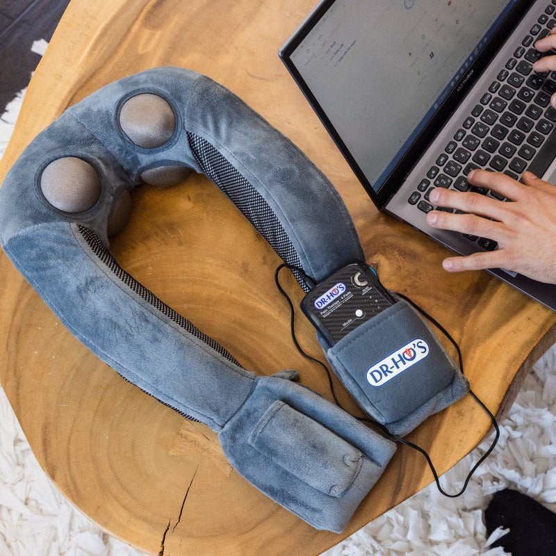 DR-HO'S Neck Therapy Pro pillow unit and control device resting on a table beside a laptop