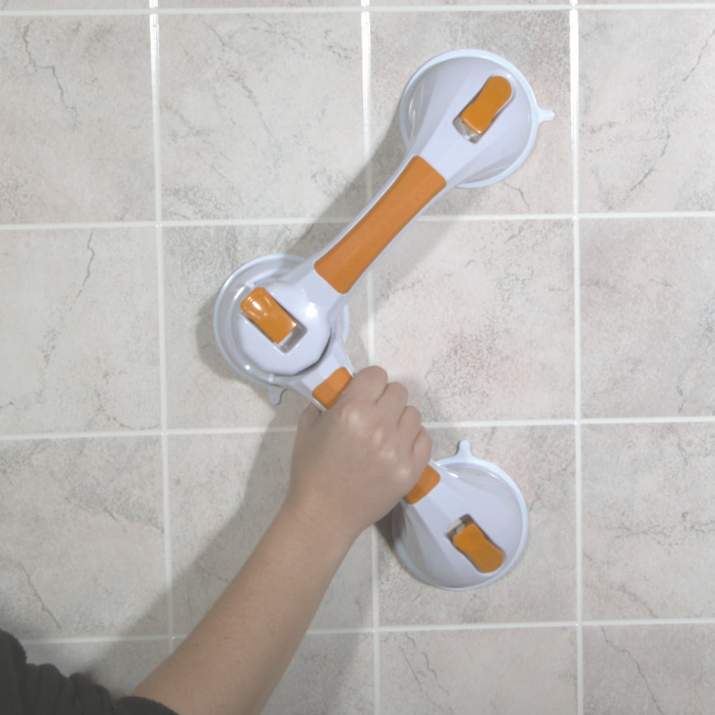 Hand holding a white and orange Drive Medical rotating suction cup grab bar mounted on a tiled shower wall.