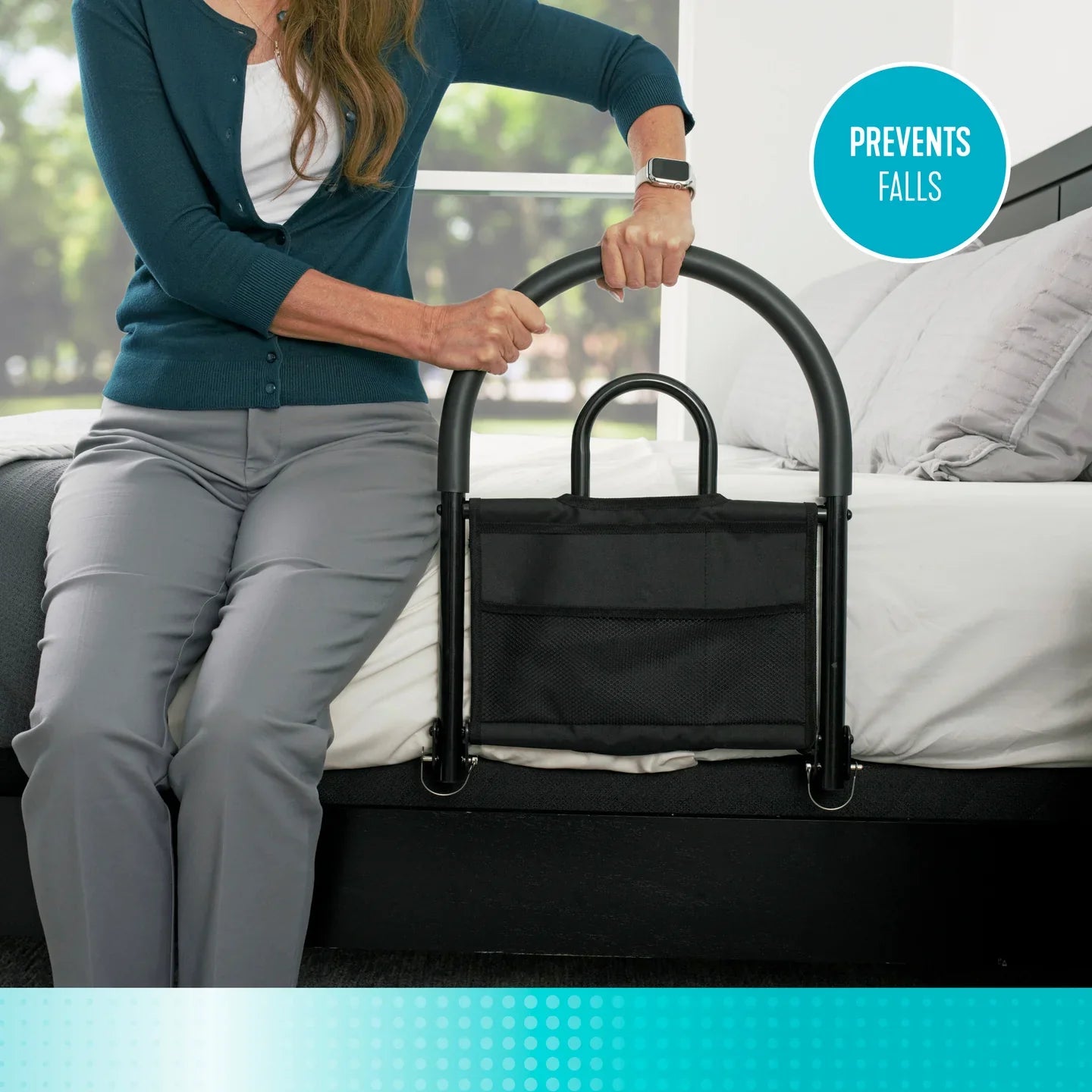 Woman sitting on the edge of a bed holding onto a black Stander Bed Rail Advantage Traveler assist handle with organizer pouch, featuring a circular badge reading Prevents Falls.