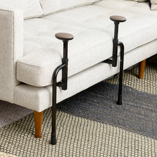 Stander EZ Stand-N-Go couch assist standing frame with dual padded grab handles fitted around the cushion of a beige sofa on a patterned rug.