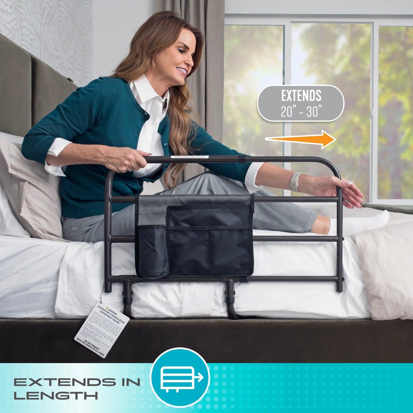 Woman sitting on a bed adjusting a black Stander Wonder Bed Rail safety guard extending in length from 20 to 30 inches, featuring an orange directional arrow and a teal bottom banner reading EXTENDS IN LENGTH.