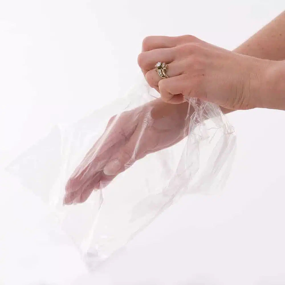 A close-up of a hand inside a clear disposable plastic liner, ensuring a sanitary and mess-free paraffin wax treatment experience.