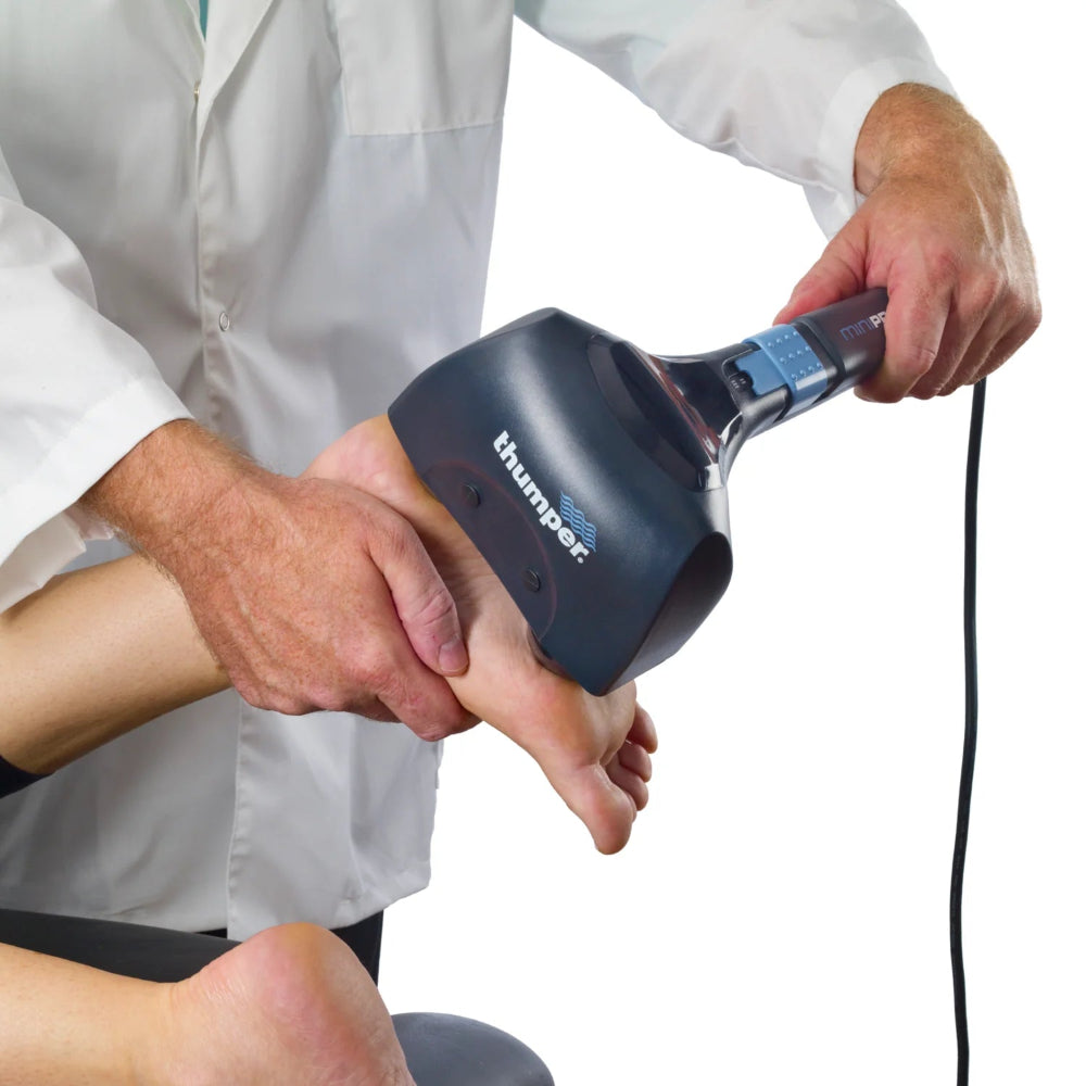A user applying the Thumper Mini Pro to the bottom of their foot for a deep-tissue sole massage.