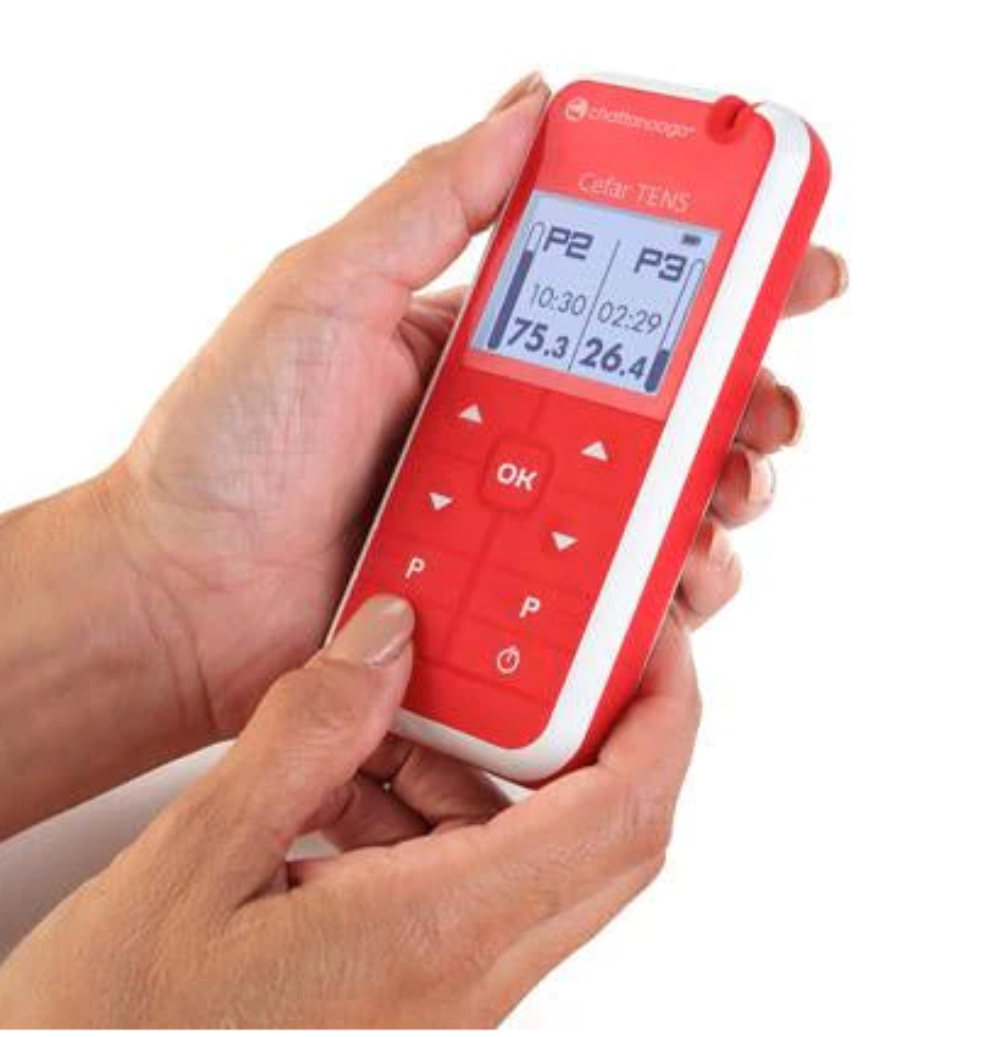 A lifestyle shot showing the Chattanooga Cefar TENS unit held in a hand, highlighting its compact, ergonomic design and large digital display for easy parameter monitoring.